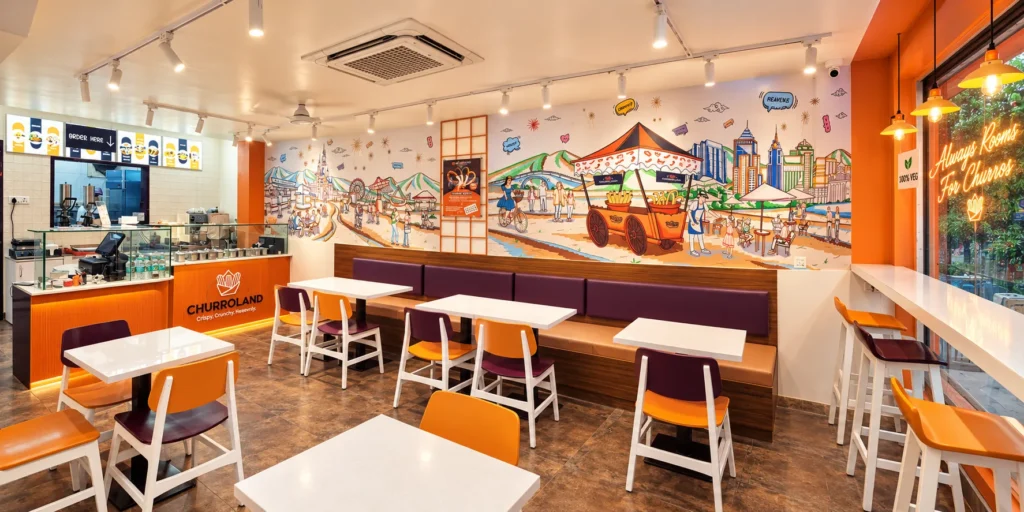 Inside Churroland Koramangala: dine-in seating with a hand-painted Bengaluru and churro cart mural